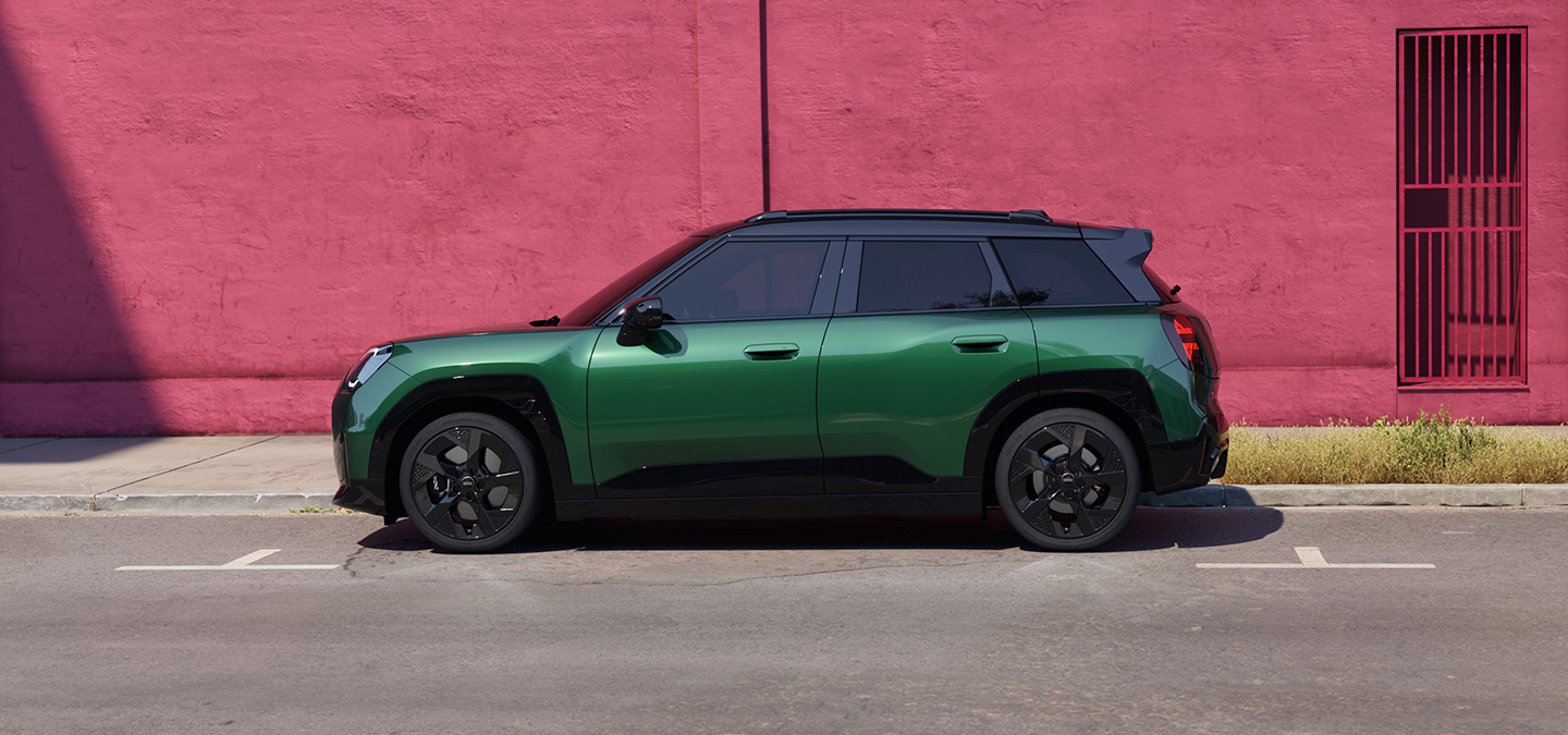 Vista lateral derecha del MINI Aceman 100 % eléctrico en British Racing Green con techo negro en una calle.