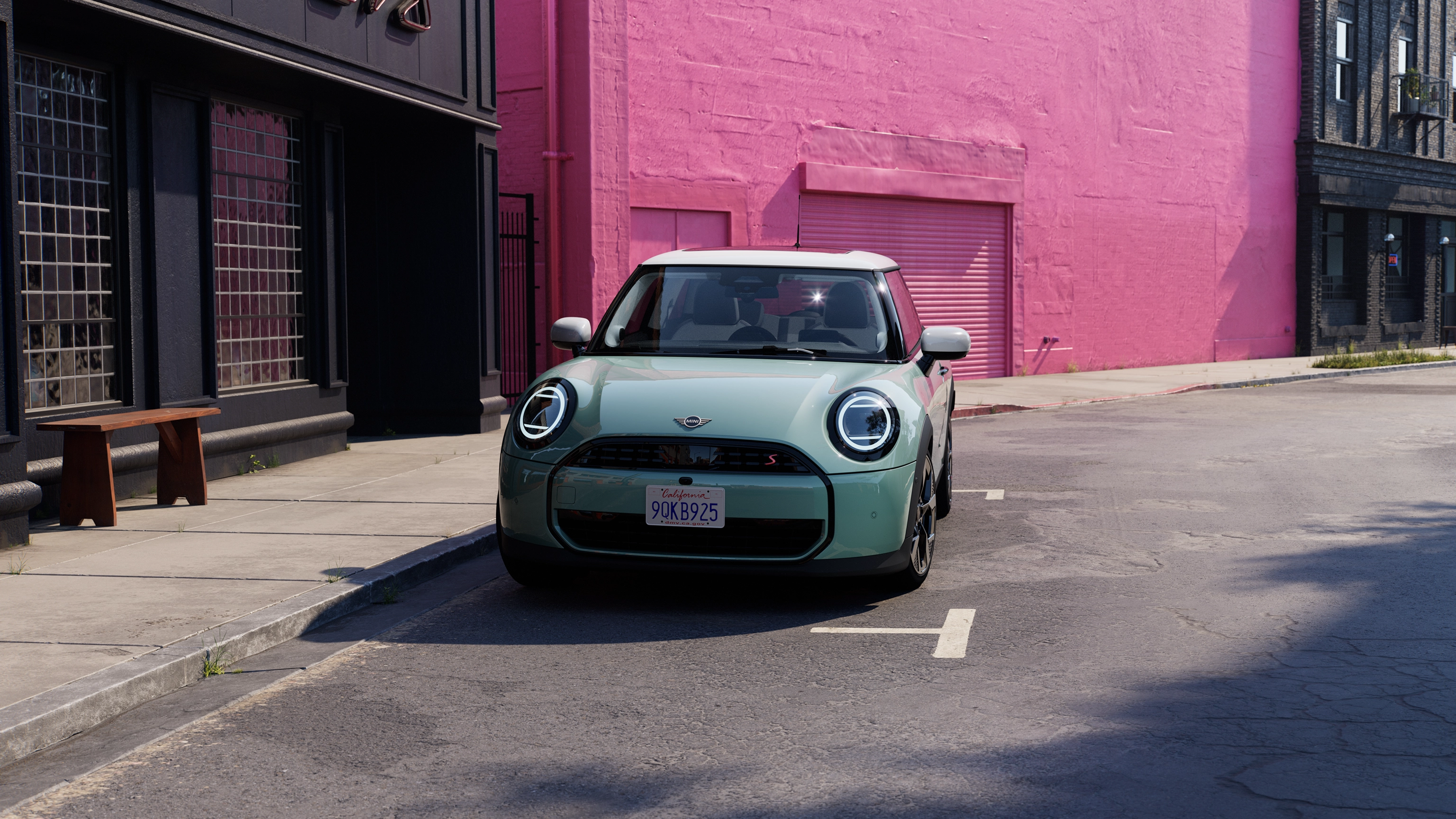Vista frontal del MINI Cooper en Ocean Wave Green con techo blanco aparcado en la calle con una pared rosa de fondo