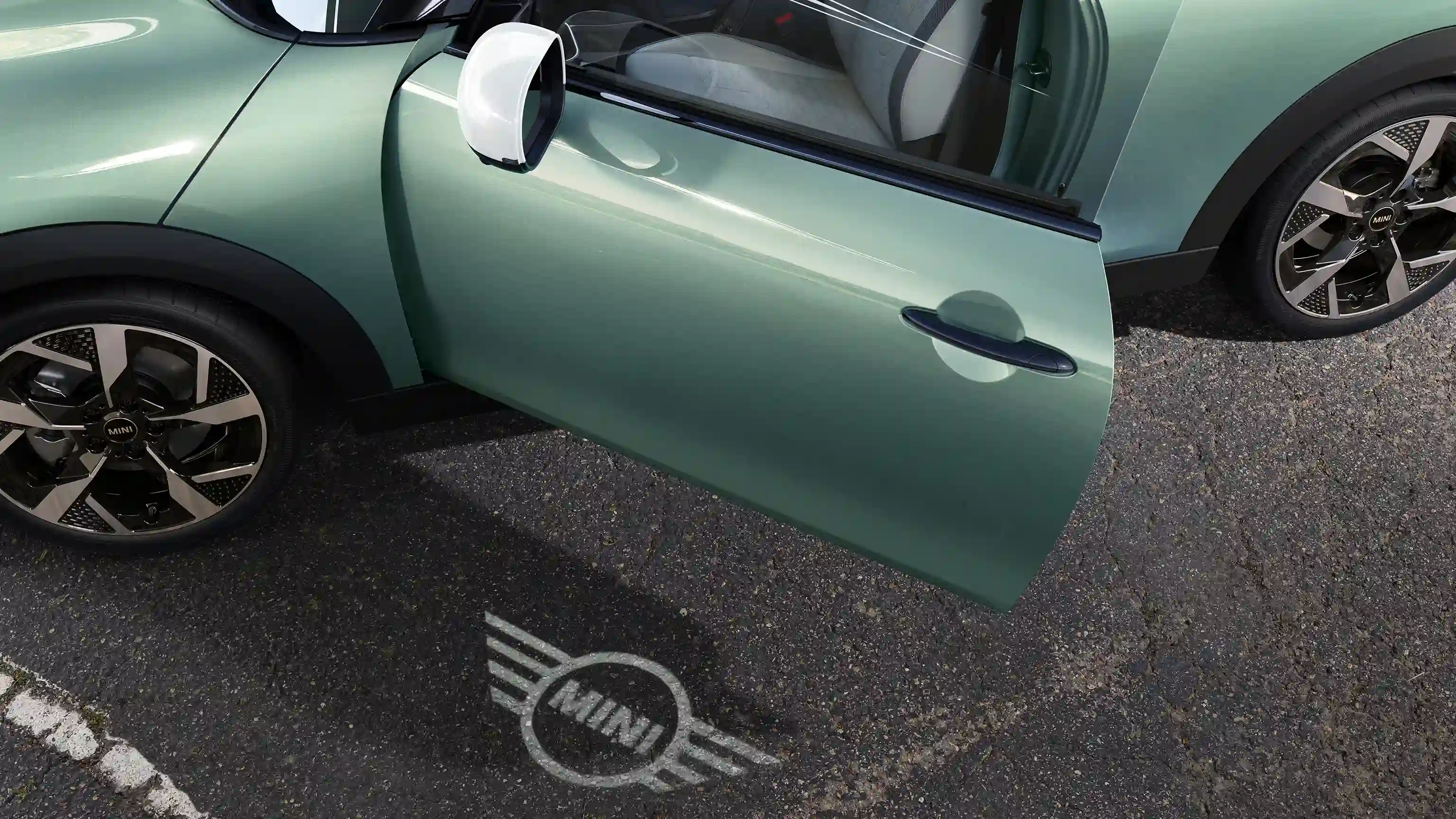 Vista exterior del MINI Cooper con la puerta abierta y la luz de bienvenida con el logo MINI en el suelo 