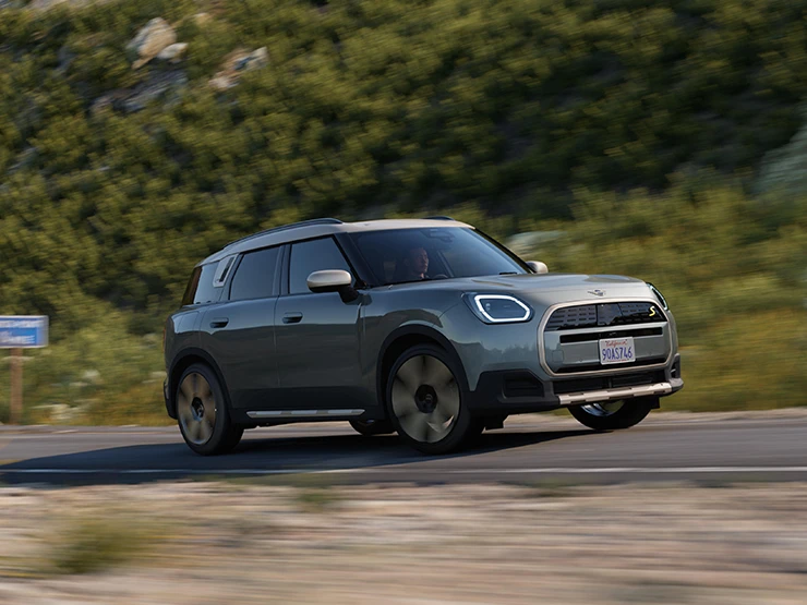 Vista lateral del MINI Countryman 100 % eléctrico en Smokey Green con techo Vibrant Silver conduciendo.