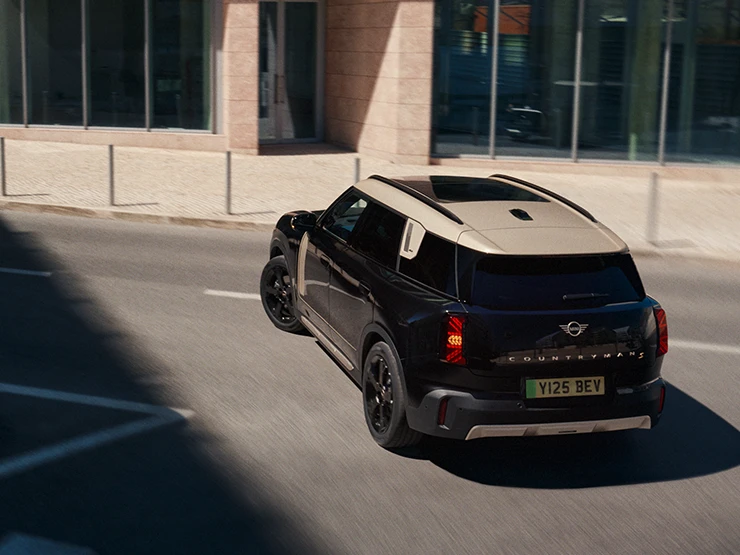 Vista posterior del MINI Countryman 100 % eléctrico en Midnight Black con techo Vibrant Silver aparcando.