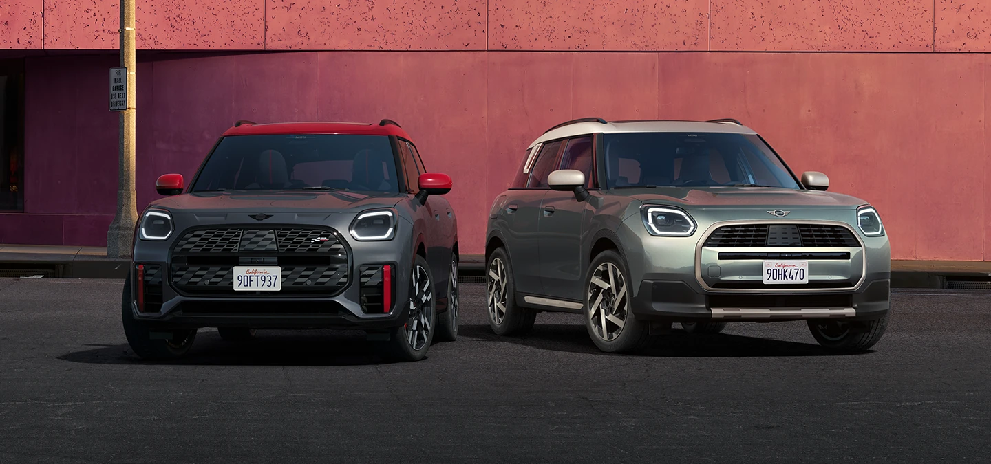 Vista frontal del MINI Countryman JCW en Legend Grey con techo rojo y del MINI Countryman en Smokey Green y techo plateado, uno al lado del otro.