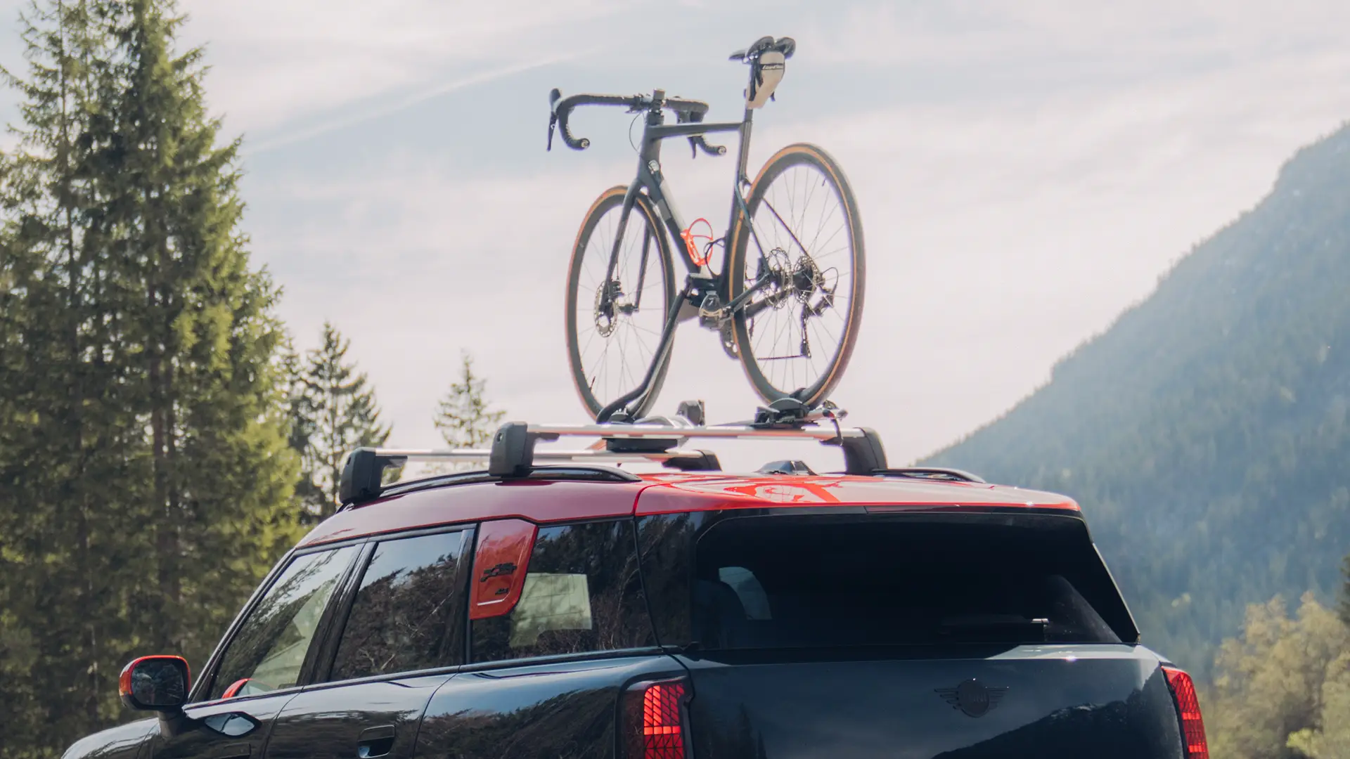 MINI Countryman Cooper en negro con portaequipajes de techo MINI y soporte para bicicletas de techo MINI con una bicicleta (vista trasera-lateral)