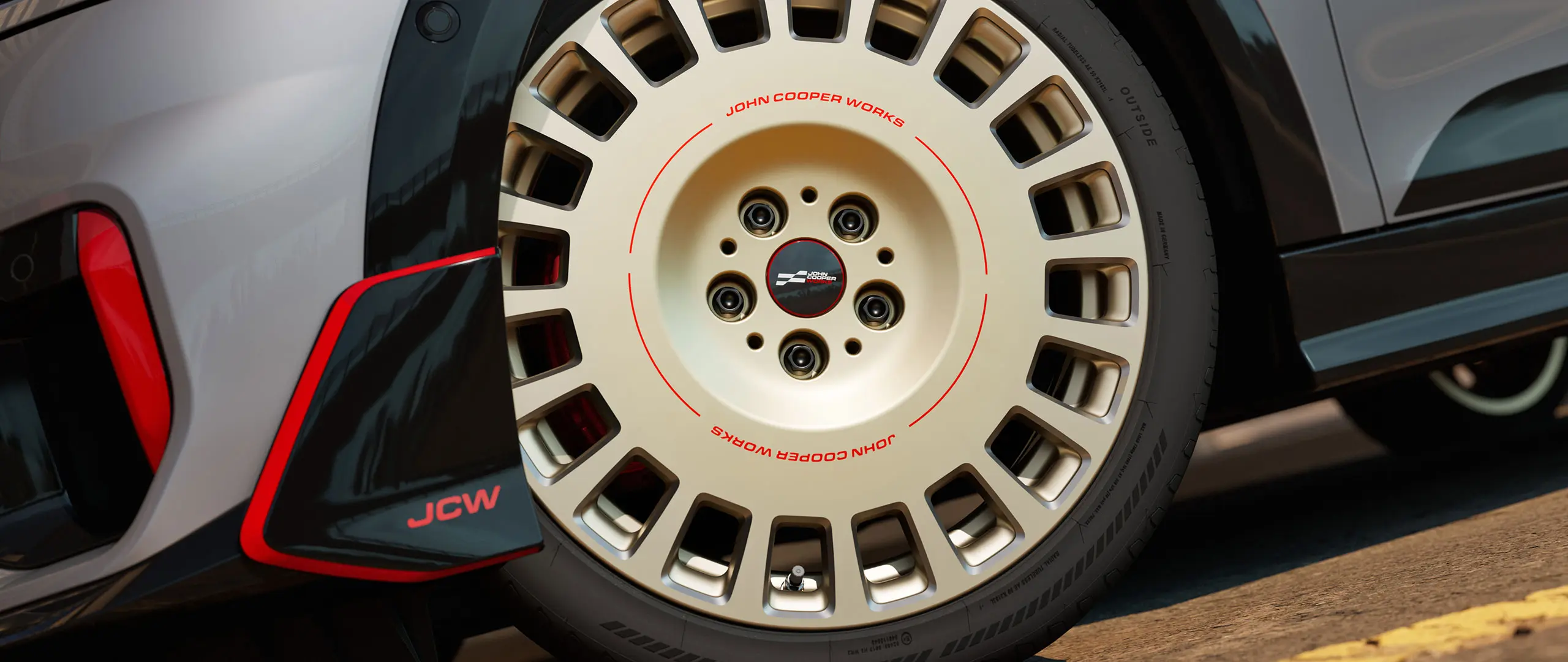 Primer plano de los detalles de una llanta JCW Rallye Spoke 964 de 18" en Bicolour Vibrant Silver y diamantada y winglet delantero.