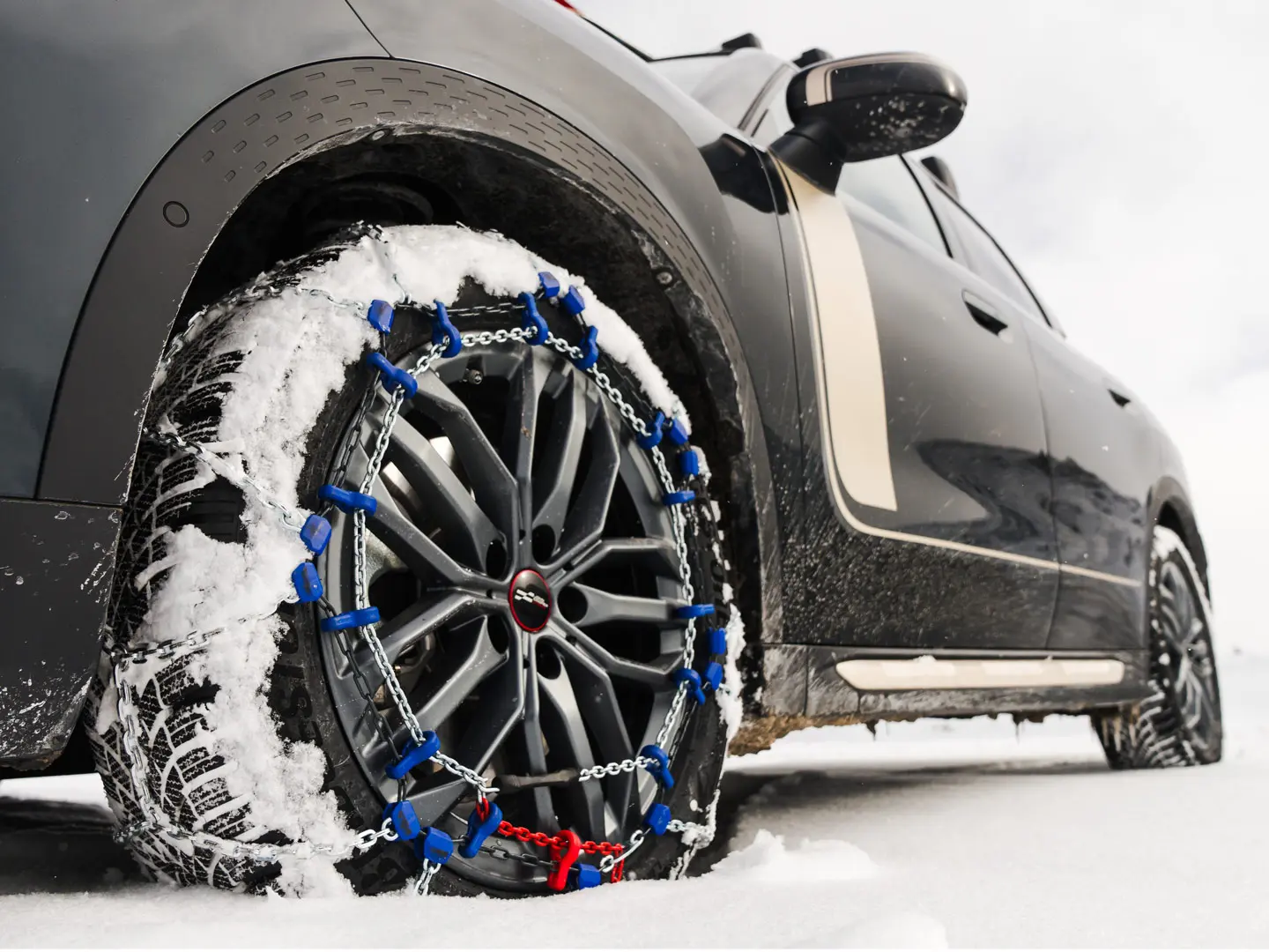Primer plano de una cadena para neumáticos instalada en la rueda de un MINI Countryman para una tracción adicional al conducir por nieve intensa. 
