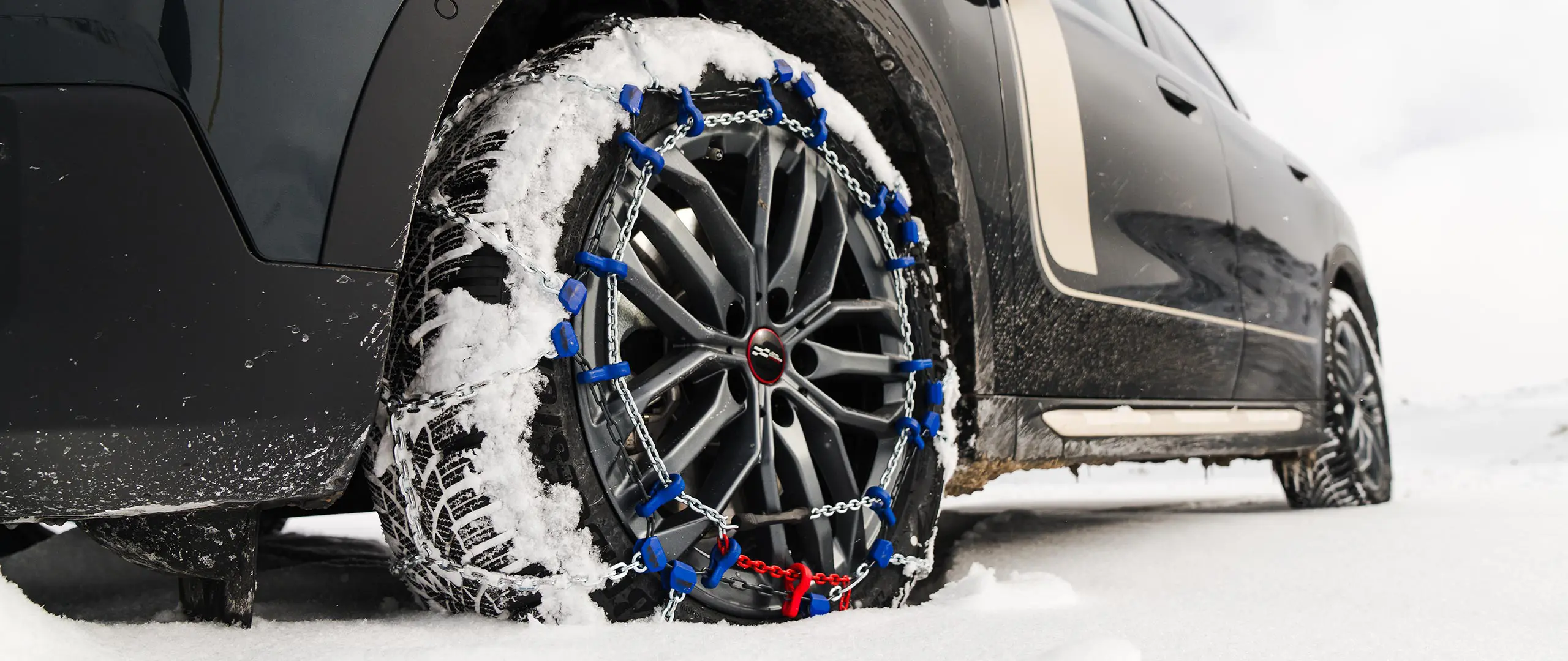Primer plano de una cadena para neumáticos instalada en la rueda de un MINI Countryman para una tracción adicional al conducir por nieve intensa. 