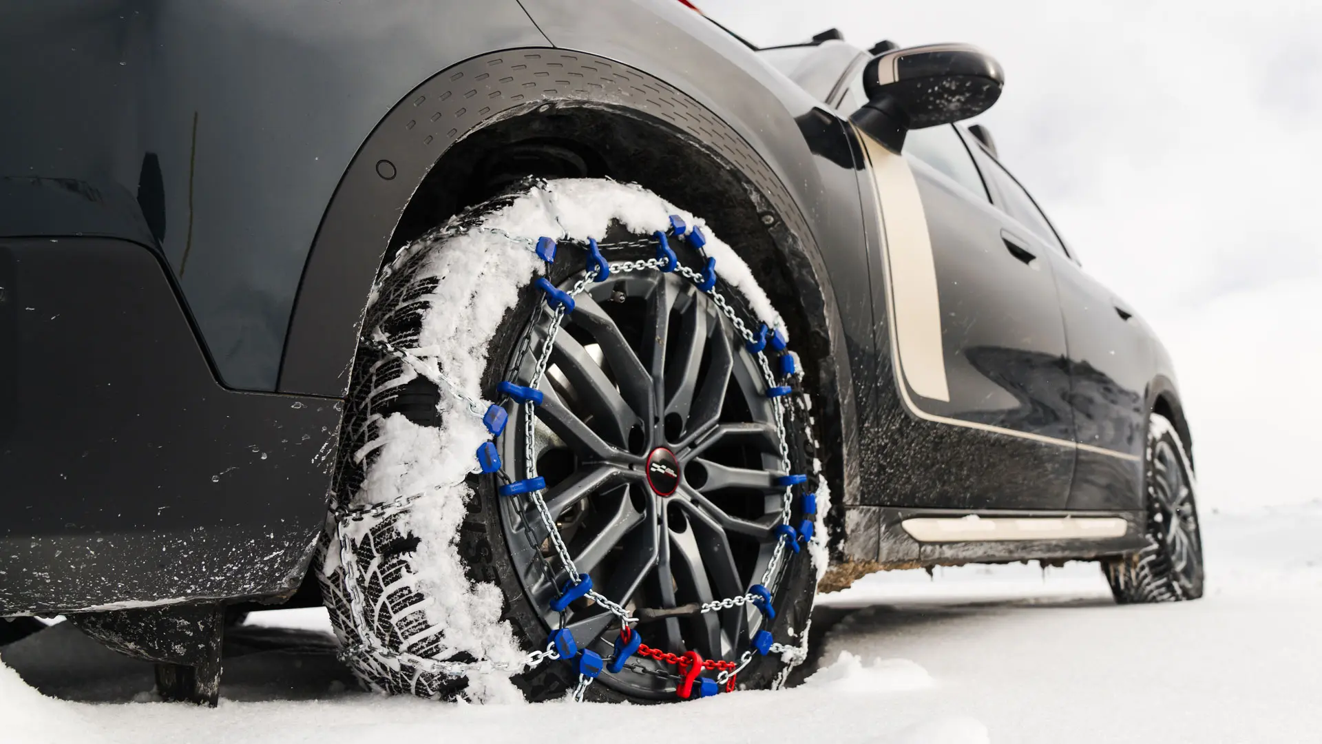 Primer plano de una cadena para neumáticos instalada en la rueda de un MINI Countryman para una tracción adicional al conducir por nieve intensa. 