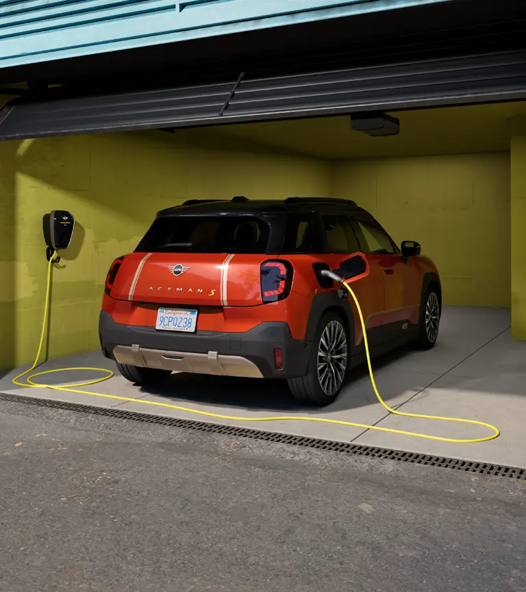 MINI Aceman S eléctrico cargando conectado a un MINI Wallbox Plus, vista trasera, aparcado en un garaje.