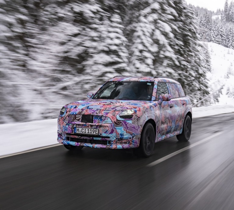 Nuevo MINI Countryman 100% eléctrico camuflado circulando por una carretera en un entorno nevado.