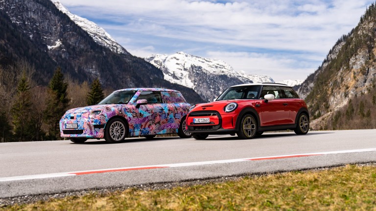 The new MINI Cooper Electric of the new MINI family and the current MINI Cooper SE stand side by side on the road.