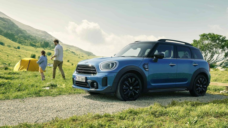 Dreiviertelansicht der MINI Highlands Edition von der Seite auf einer Landstrasse stehend vor dem Mann und der Frau wie sie zum Zelt gehen